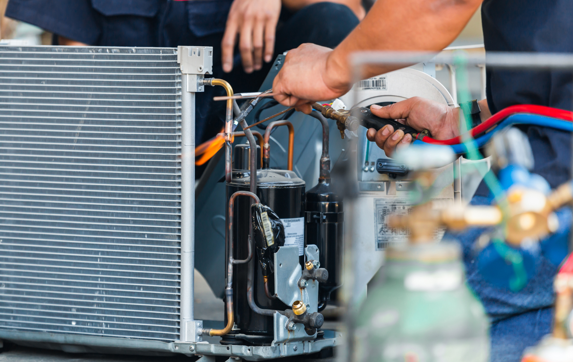 HVAC technician repairing an air conditioning unit; uses a tool near copper pipes and a compressor.