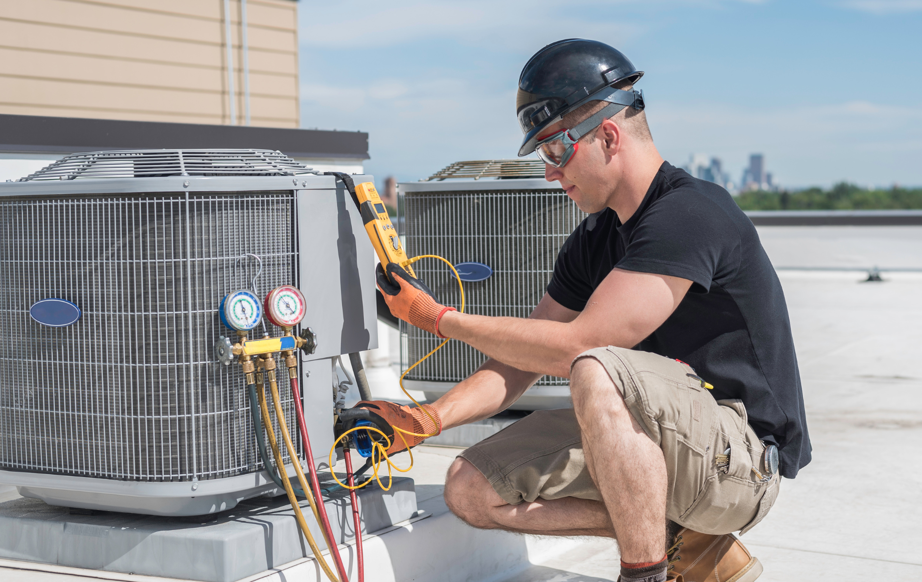 HVAC technician in safety gear inspecting rooftop air conditioning unit, using gauges.