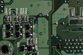 Close-up of a green circuit board with electronic components, including resistors and capacitors labeled with identifiers.