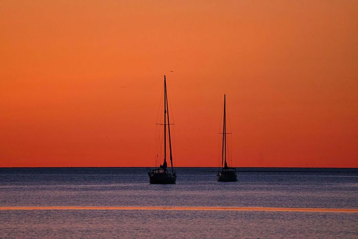 Two sailboats are in the ocean at sunset.