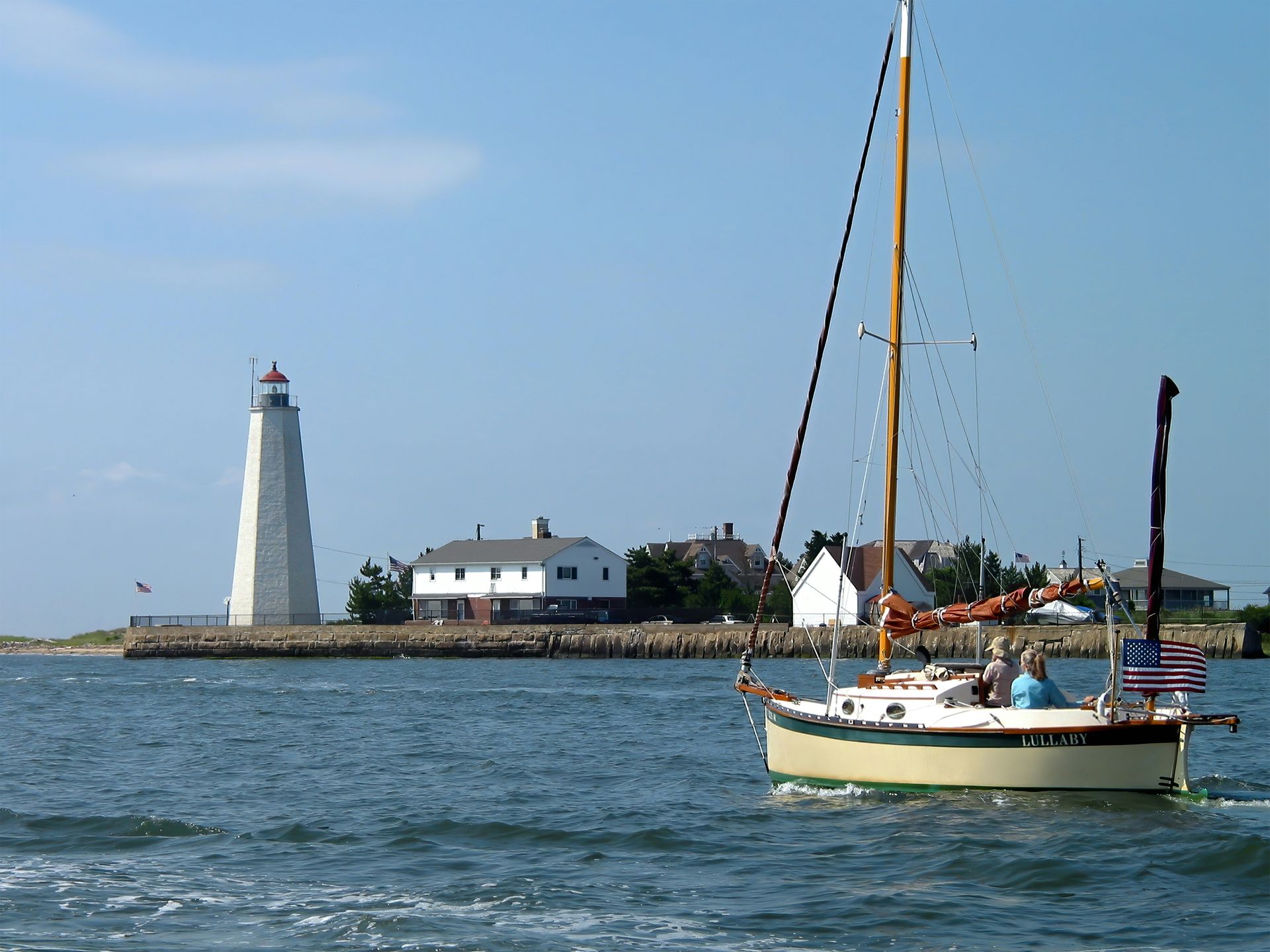 A sailboat in the water with a lighthouse in the background