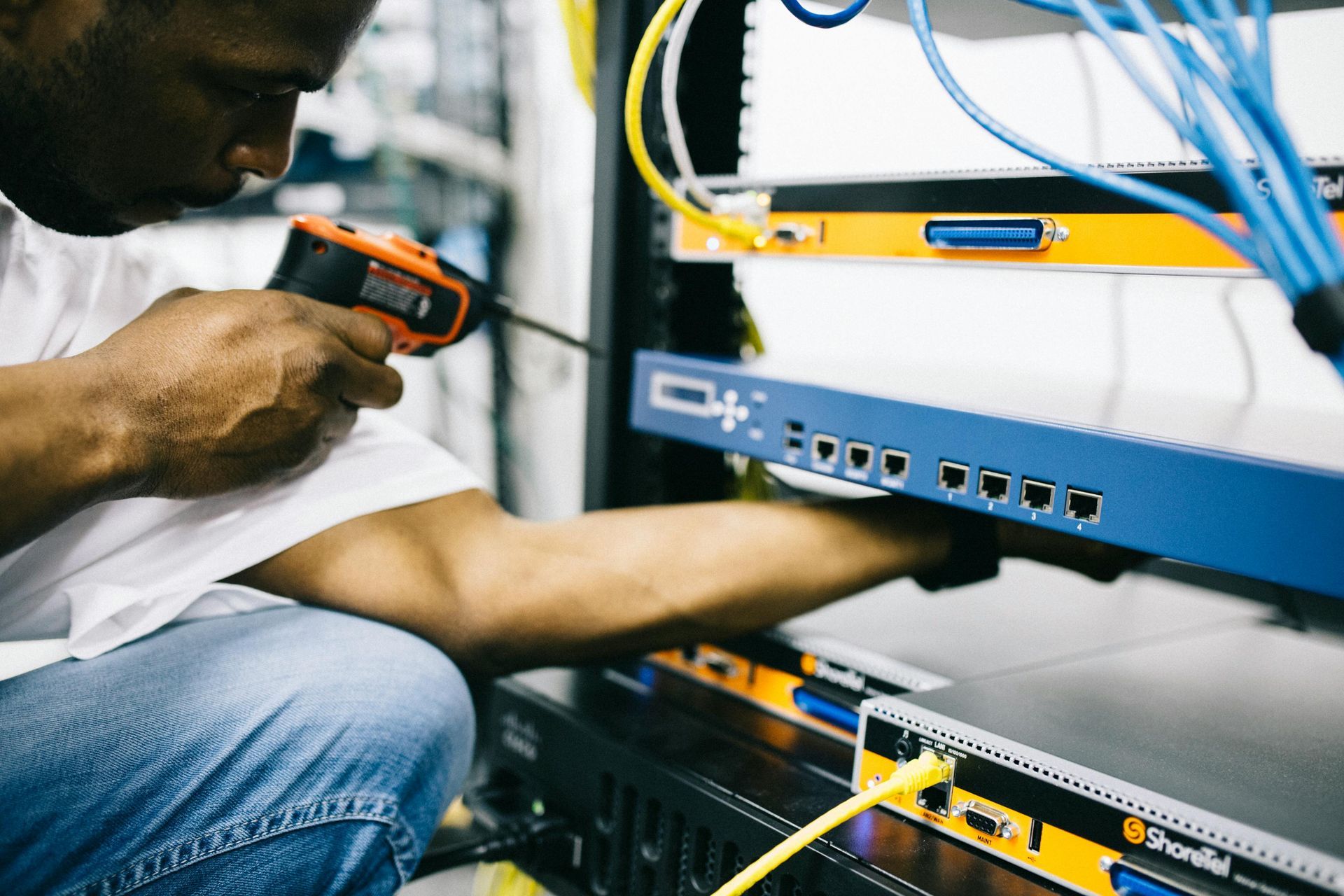 Technician using a drill to install cables in a server rack with blue network equipment