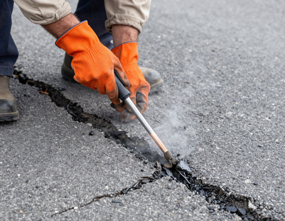 Worker filling cracks in asphalt with hot-pour filler