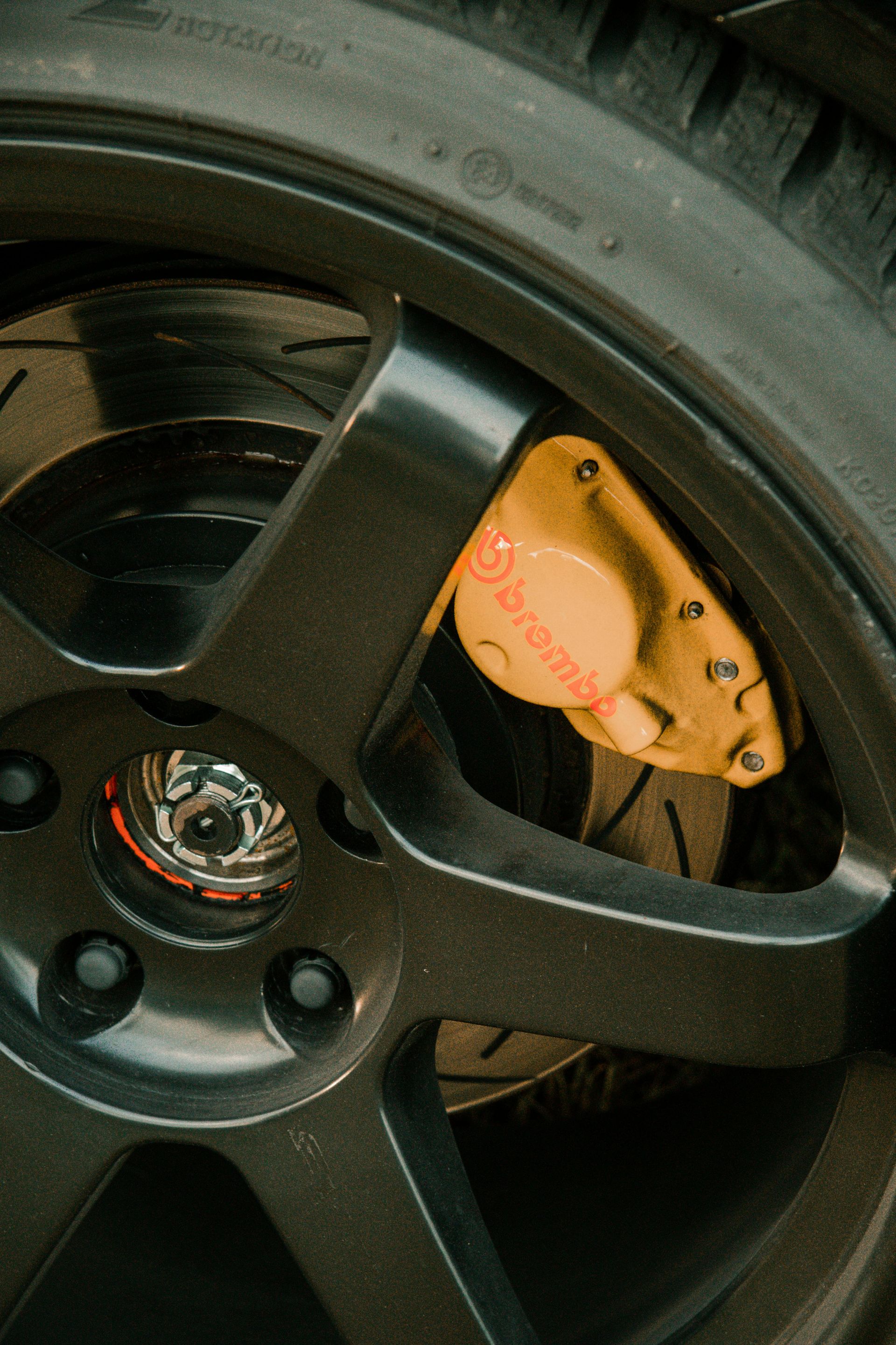 Close-up of a black car wheel with a yellow Brembo brake caliper and slotted rotor.