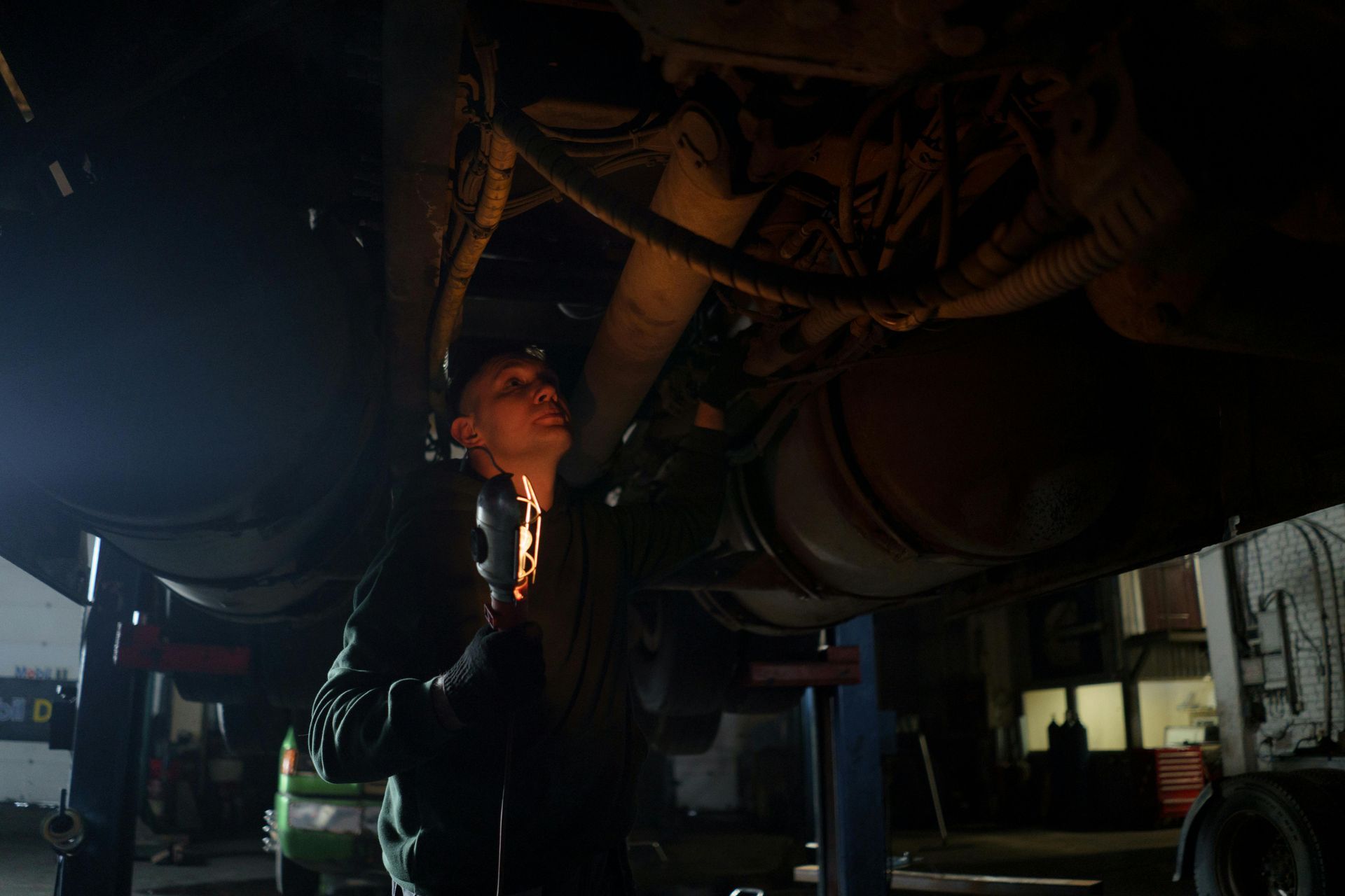 Mechanic inspecting under a truck, using a flashlight in a dim garage.