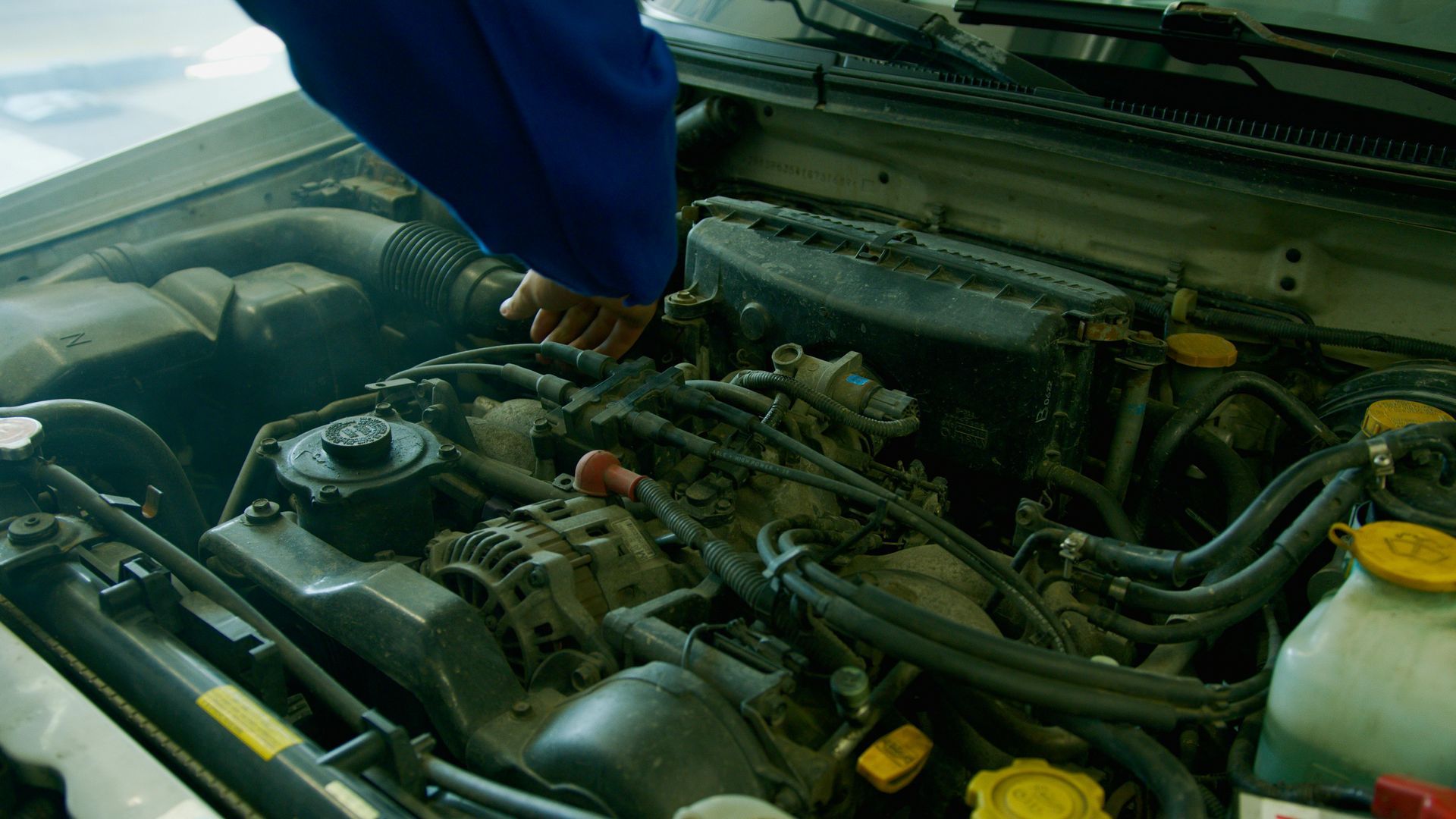 A mechanic working on a car engine, with hands touching parts under the hood.