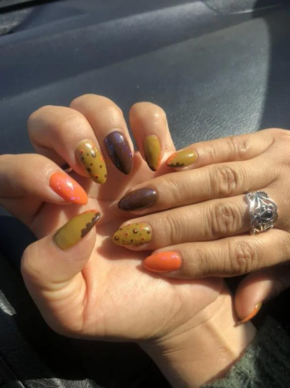 Manicured hands with almond-shaped nails in autumn colors: orange, olive, and brown, featuring leopard print accents.