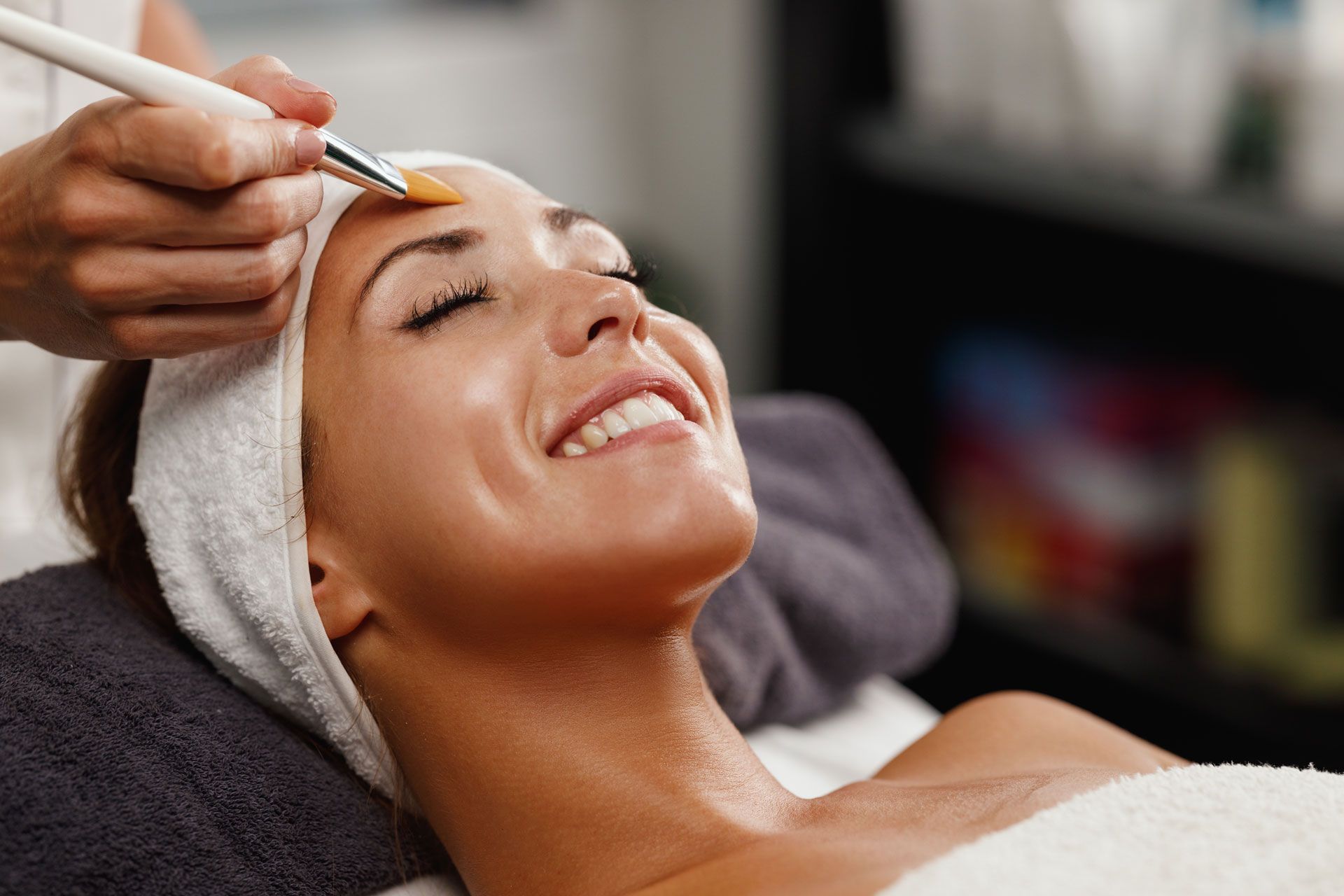 A person receiving a facial treatment with a small brush applying product to their forehead in a spa setting.