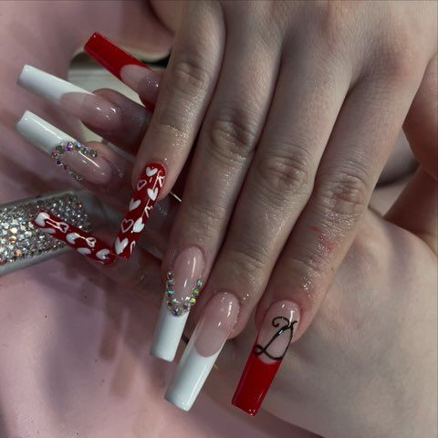 Long, square-shaped acrylic nails with red and white French tips, rhinestones, heart patterns, and a cursive letter D.
