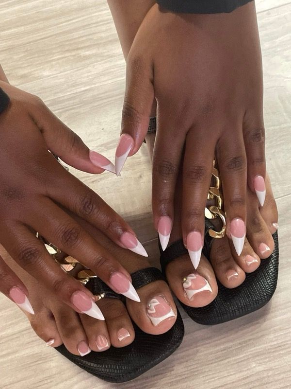 Two feet wearing black sandals and stiletto-shaped French manicure toenails with decorative white line art on big toes.