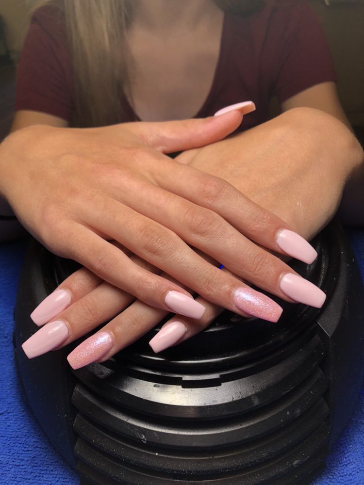 A person displays their hands resting on a black lamp, featuring long, light pink, coffin-shaped manicure.