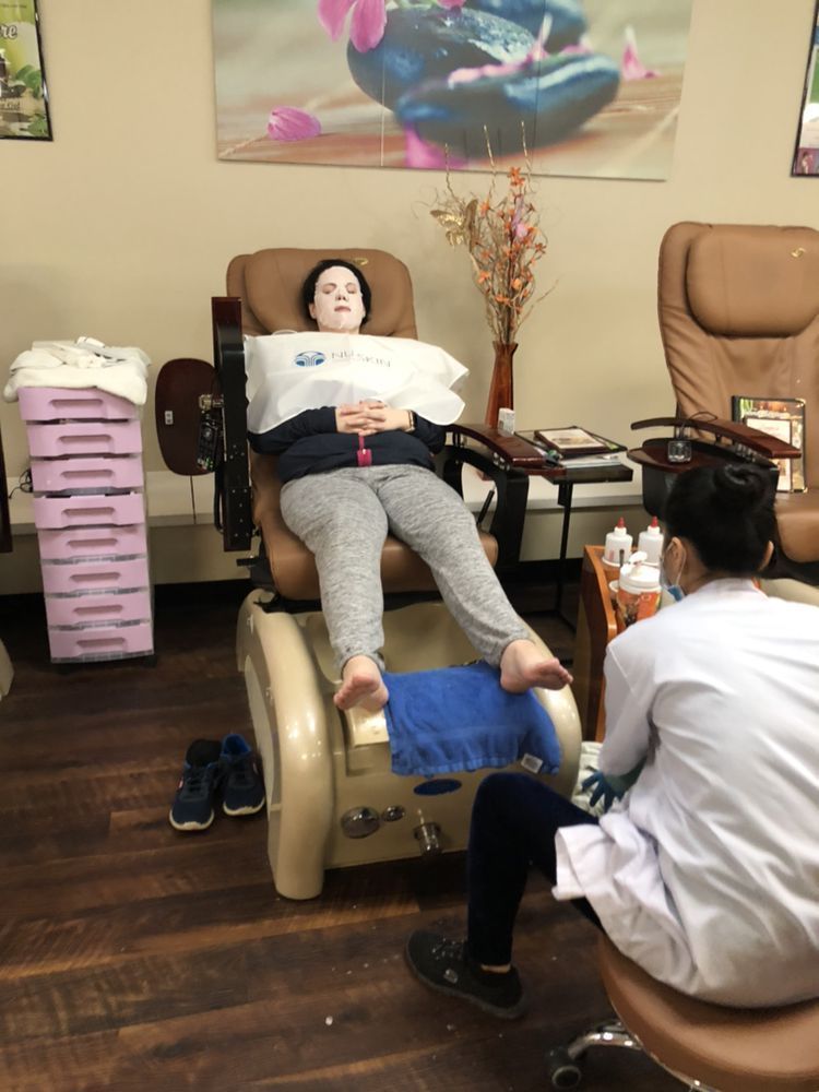 A person reclines in a pedicure chair while a technician sits across from them, preparing for a foot treatment.