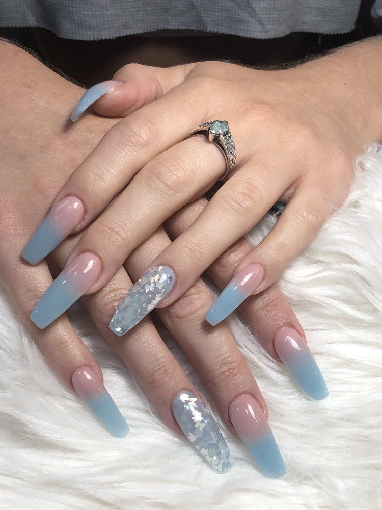 A pair of hands showcasing long, coffin-shaped nails with a blue and nude ombre gradient, accented with silver foil.