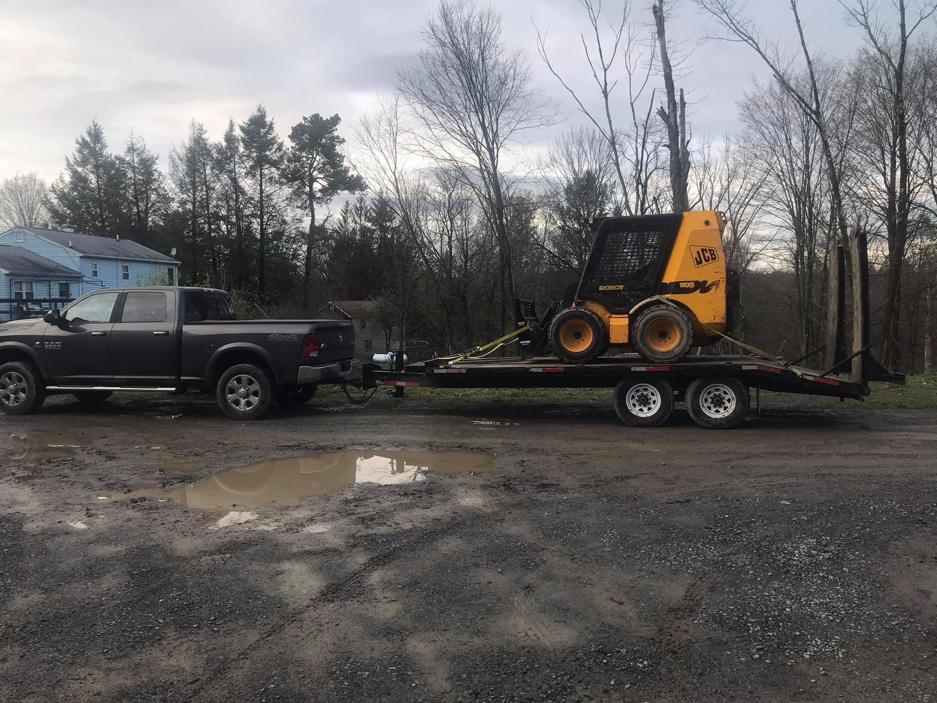 A black truck is towing a yellow tractor on a trailer.
