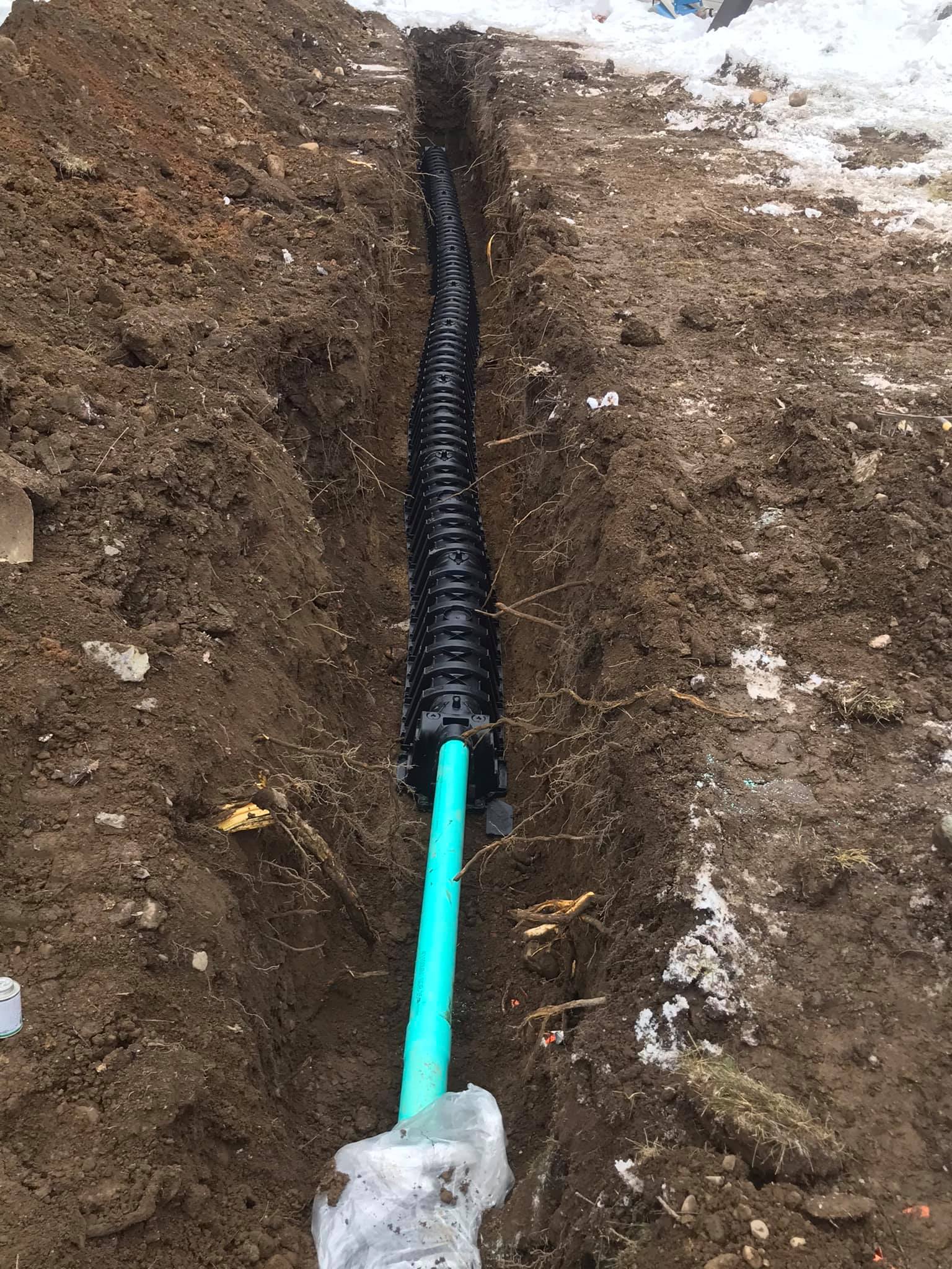 A green pipe is laying in the dirt next to a black pipe.