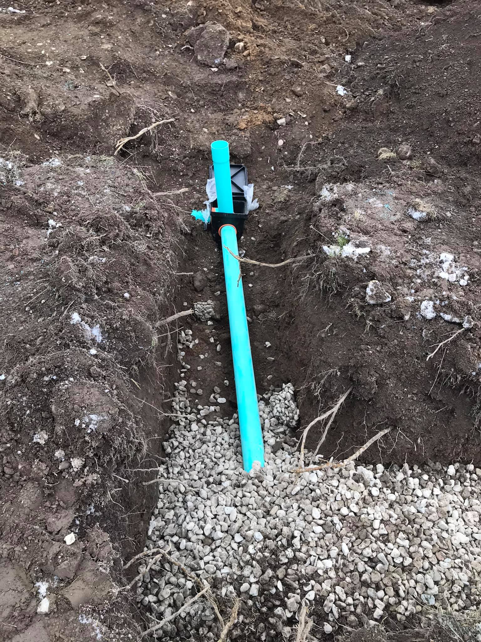 A blue pipe is sitting on top of a pile of gravel in the dirt.