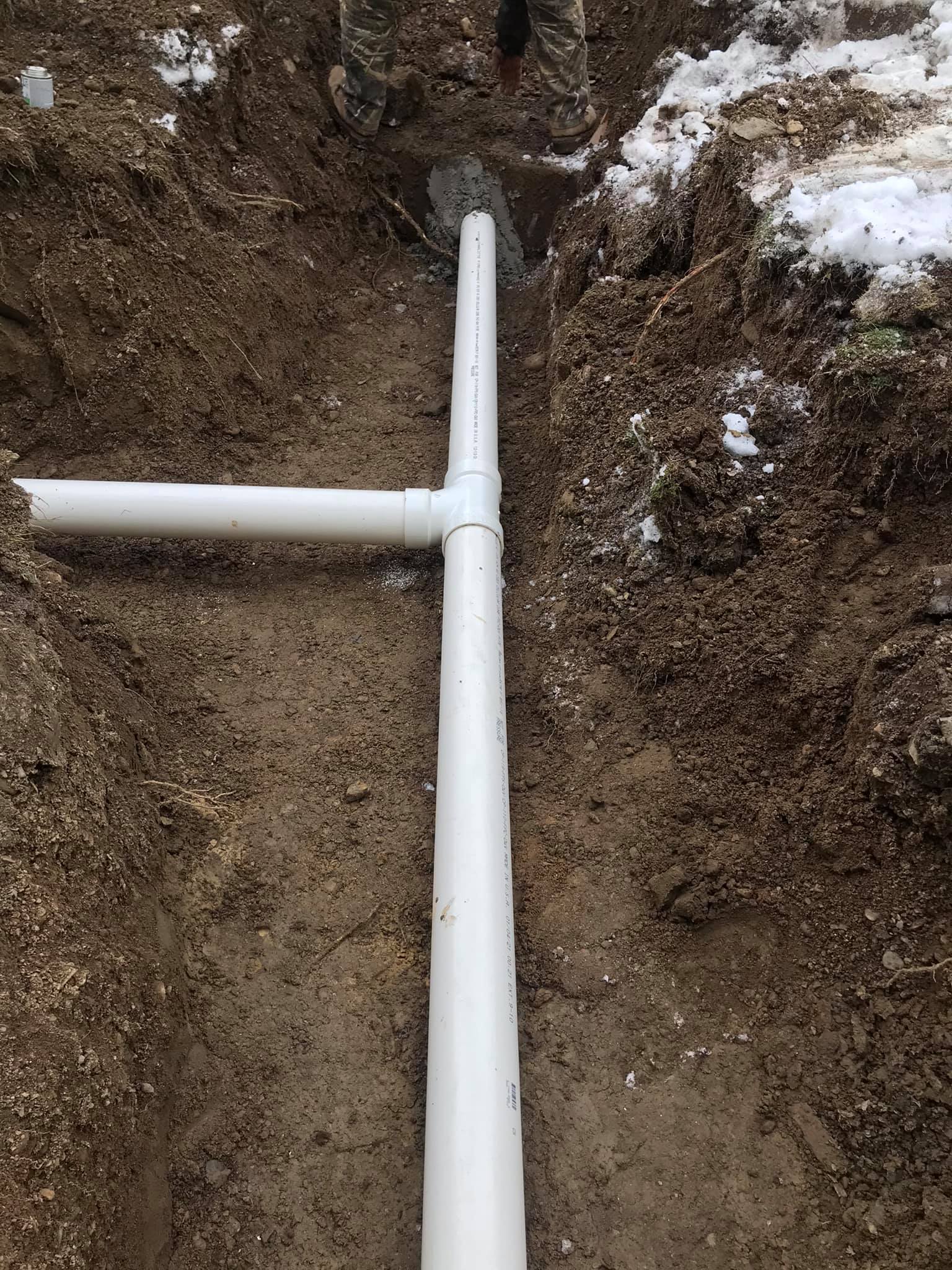 A white pipe is laying in the dirt in a hole.