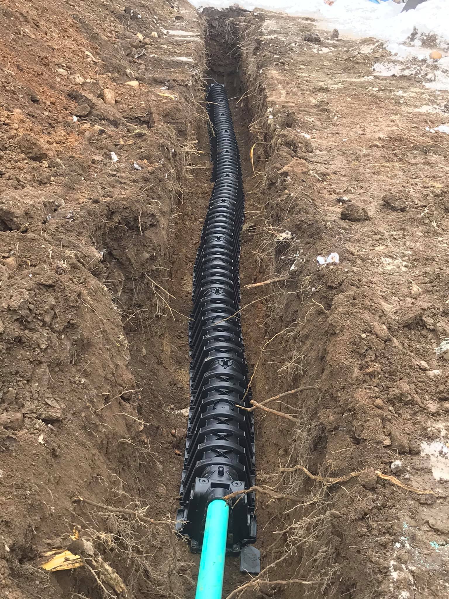 A green pipe is laying in the dirt in a trench.