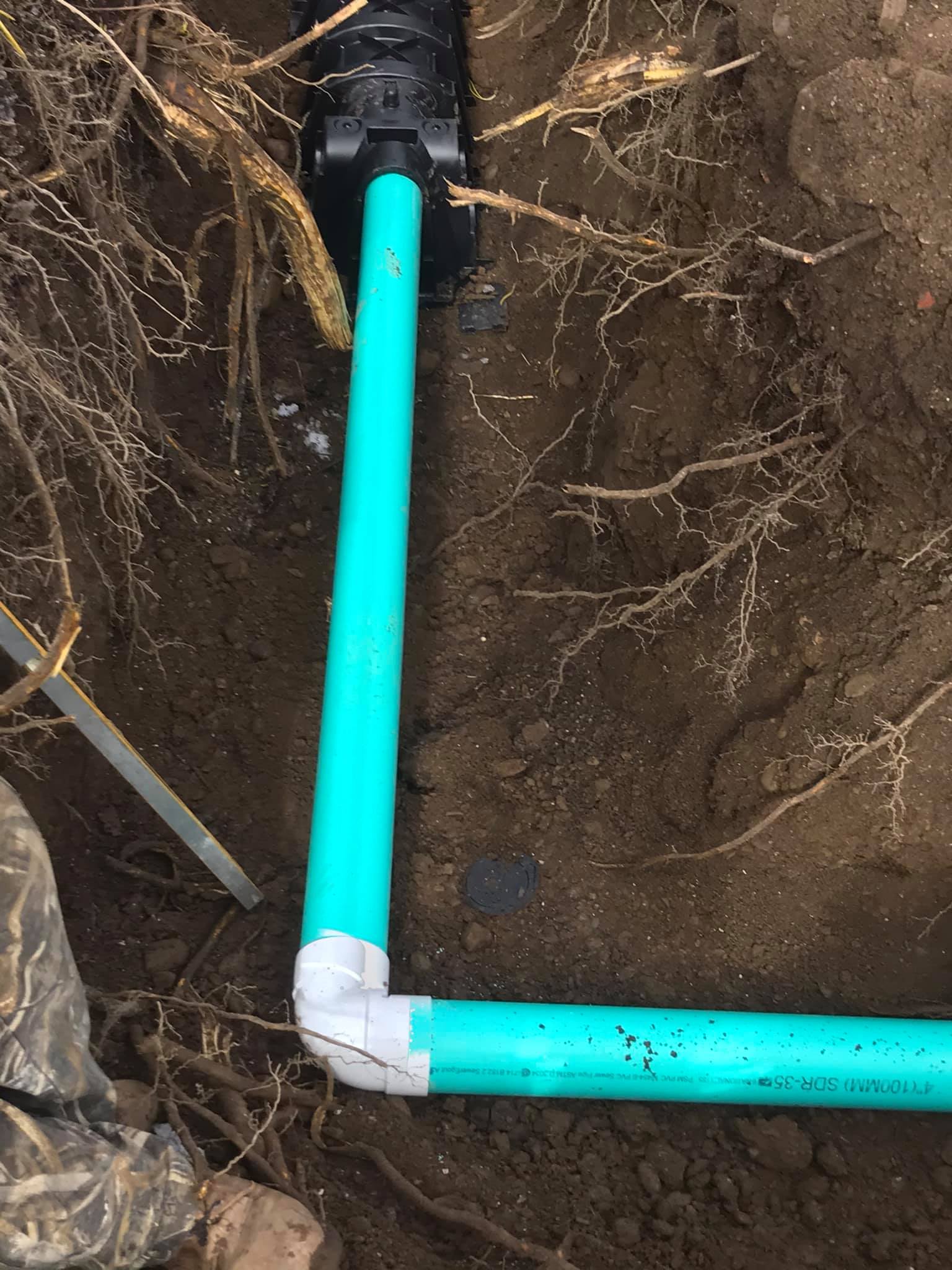 A green pipe is connected to a black pipe in the dirt.