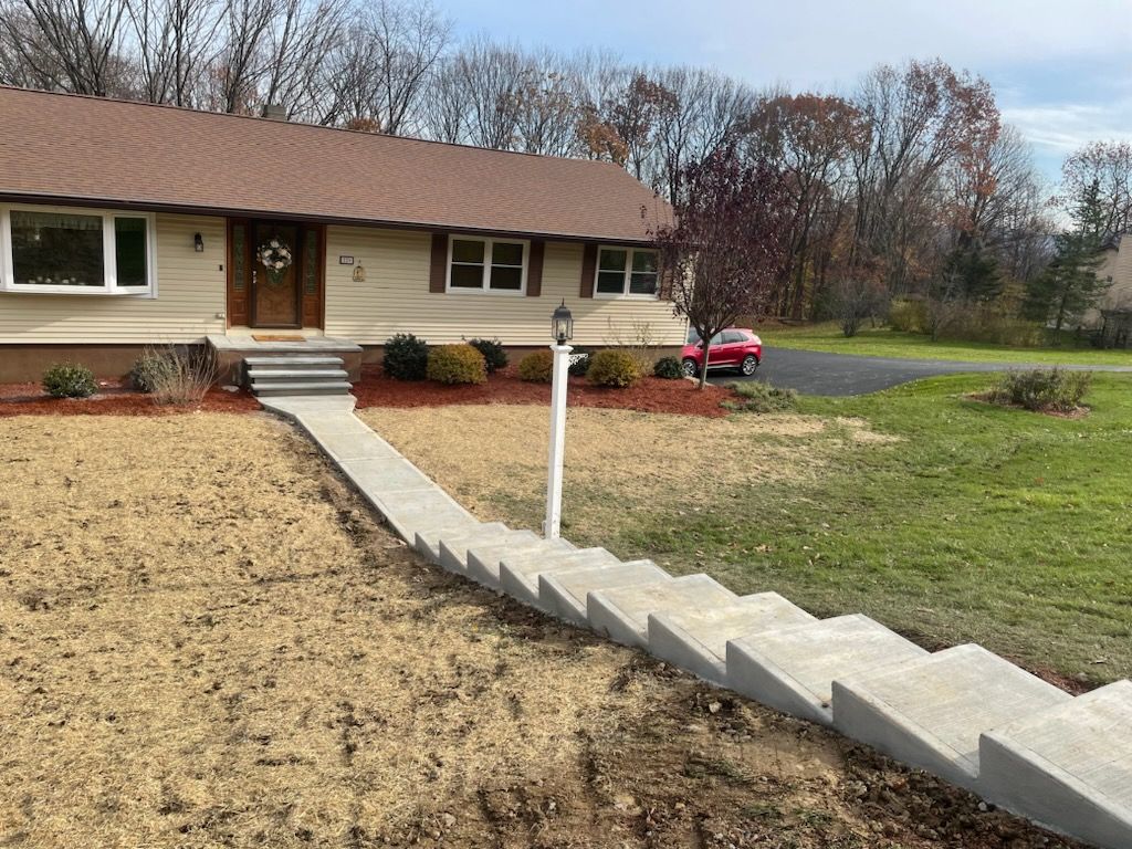 A concrete walkway leading to a house with a red car parked in front of it.