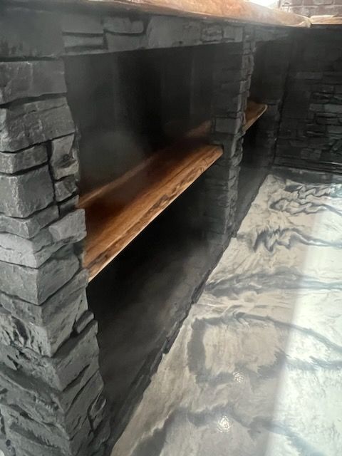 A wooden shelf is sitting next to a stone wall in a room.
