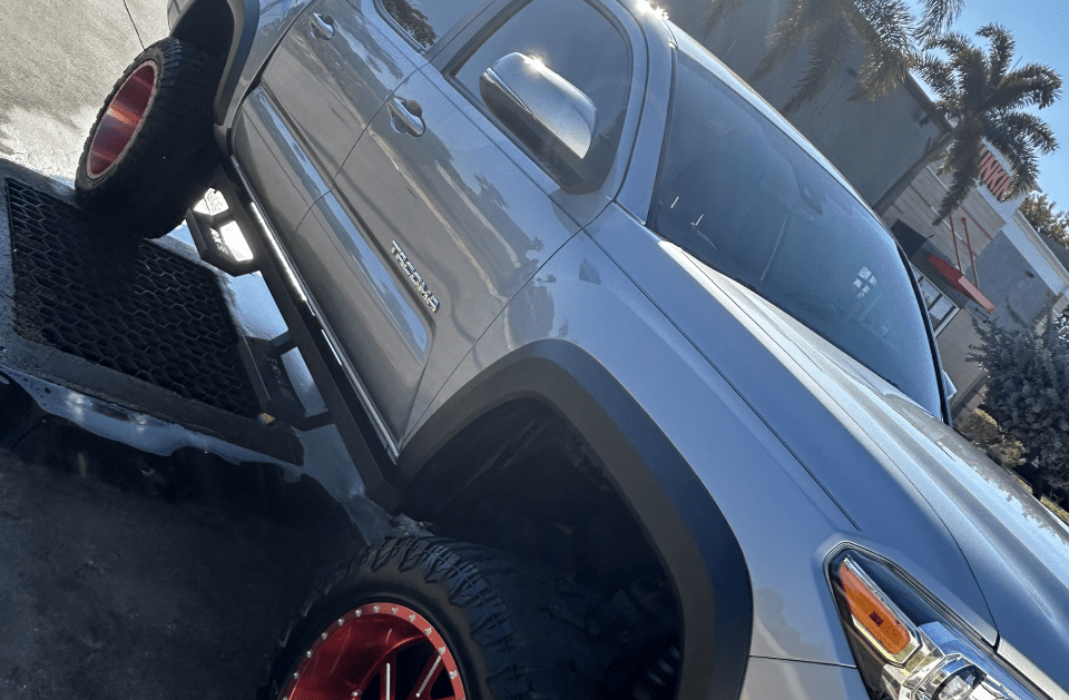 Silver Toyota Tacoma truck with red-rimmed tires parked on a grate, in a bright outdoor setting.