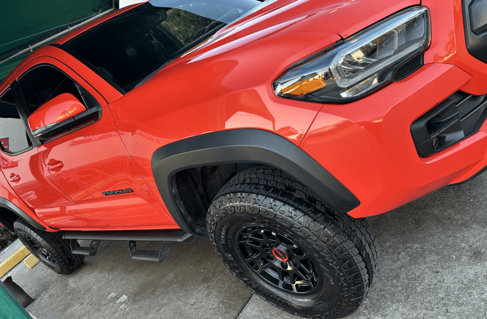 Bright orange Toyota Tacoma truck, black wheels and fender flares.