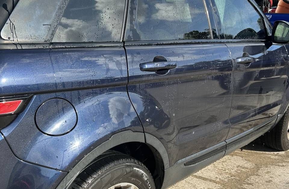 A dark blue SUV wet from being washed with water droplets on the surface.