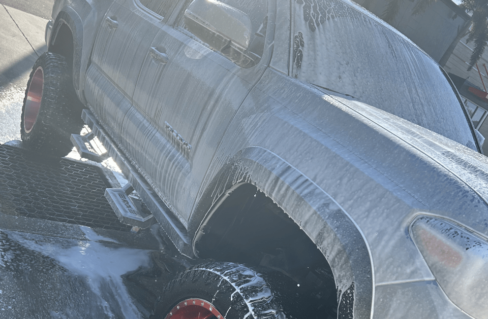 Truck covered in white foam, being washed at a carwash.