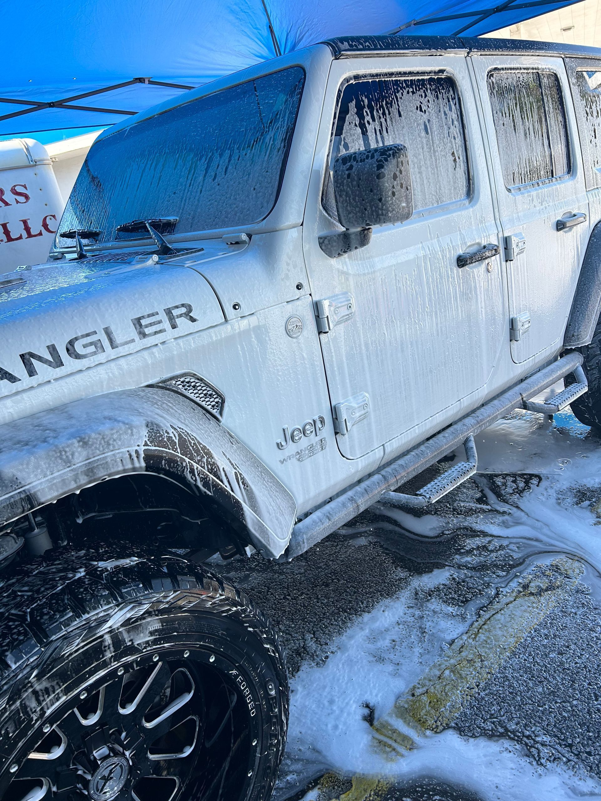 White Jeep Wrangler covered in soap suds at a car wash.