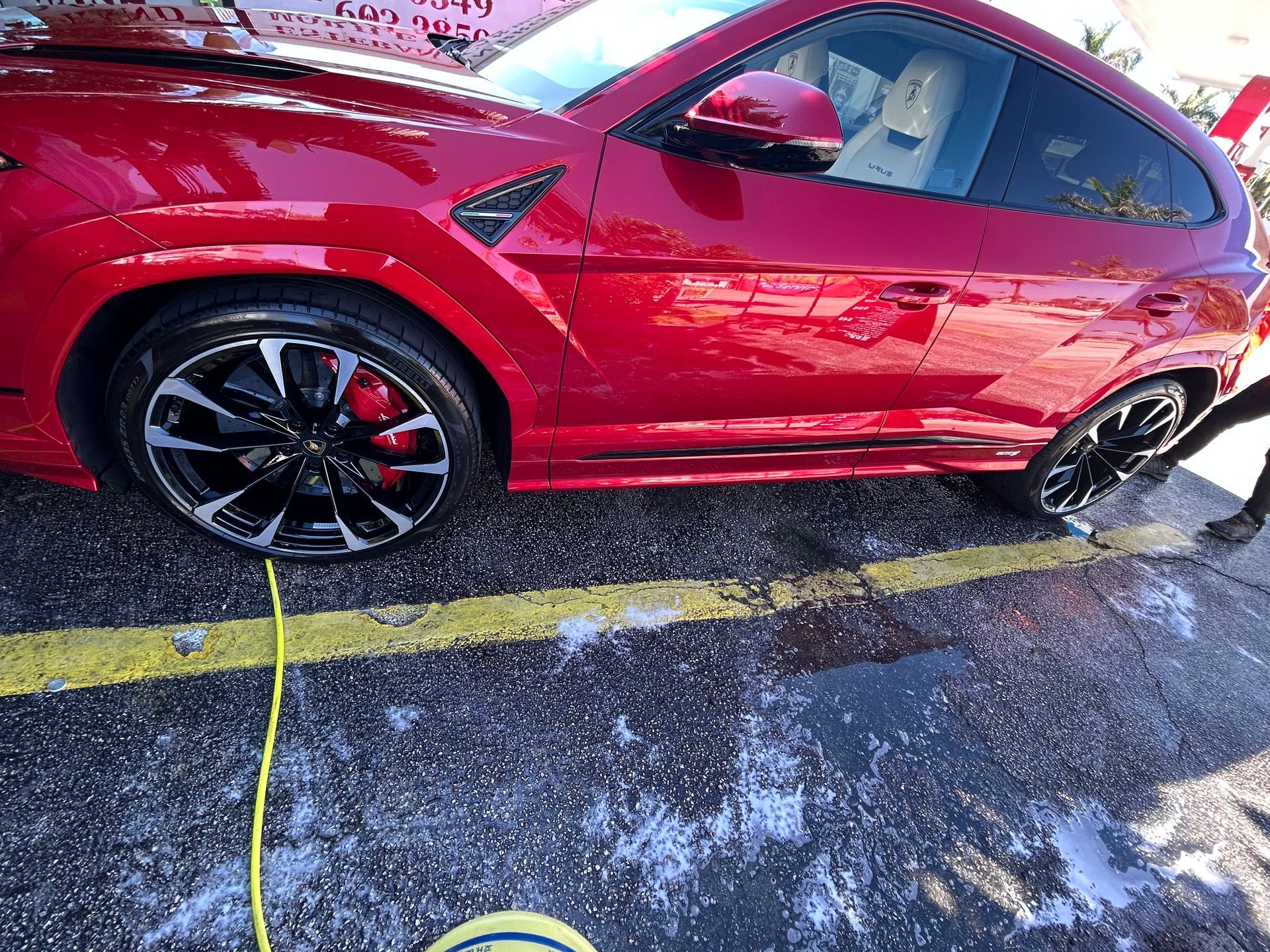 Red Lamborghini being washed, parked on a wet, concrete surface with yellow lines.