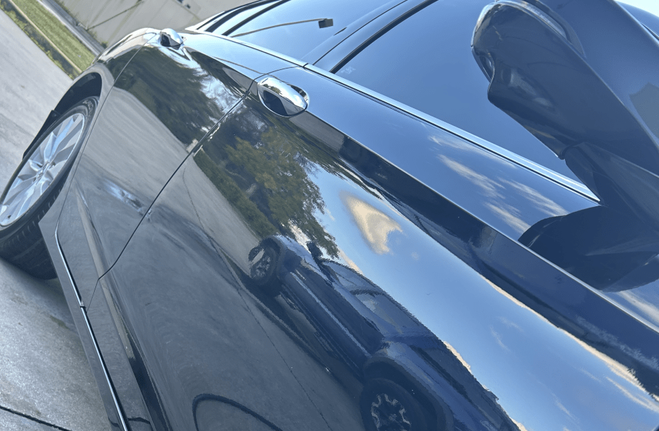Black car with tinted windows reflects surroundings on a sunny day.