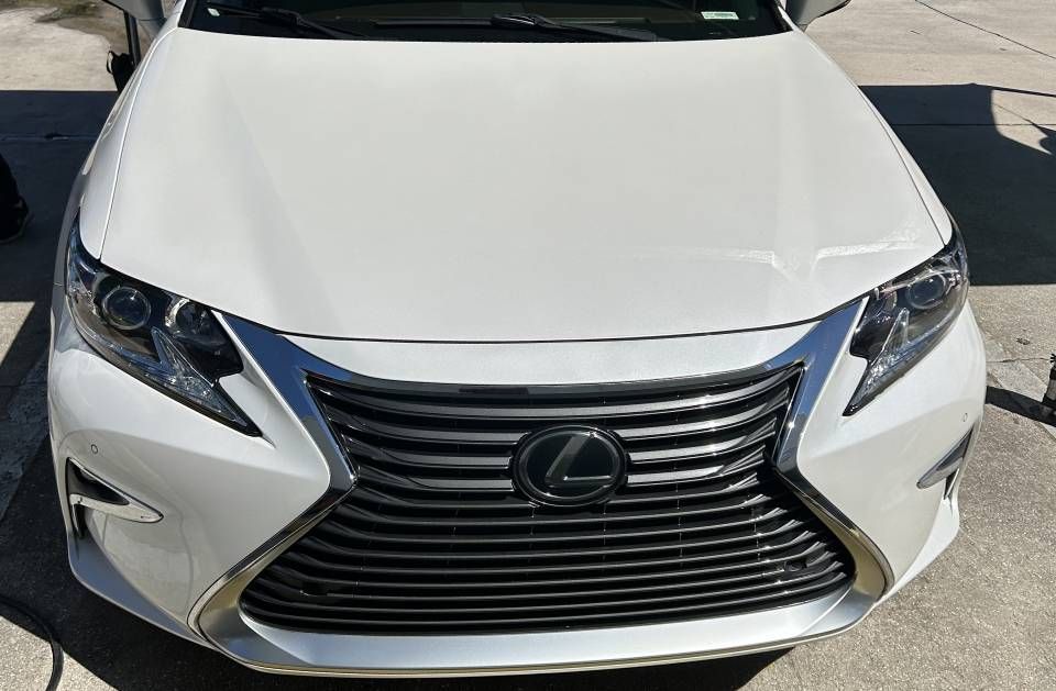 White Lexus car, front view, parked outdoors, sunny day. Chrome grille and emblem prominent.