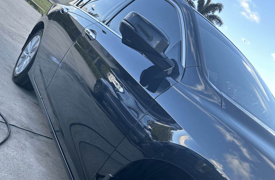 Black car parked on a concrete surface, side view, reflecting sunlight.