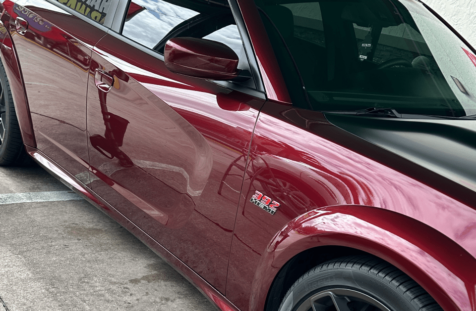 Red Dodge Charger with black hood and black rims parked on a street.