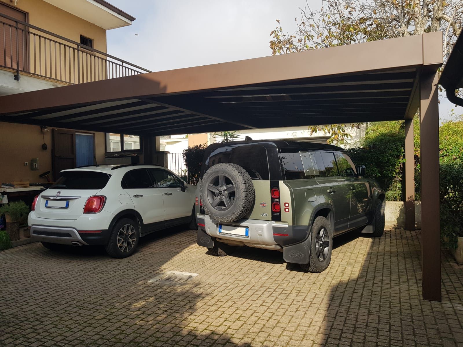 Installazione di una tettoia per auto moderna in acciaio verniciato color corten che copre due veicoli in un cortile privato, progetto Garone Serramenti.