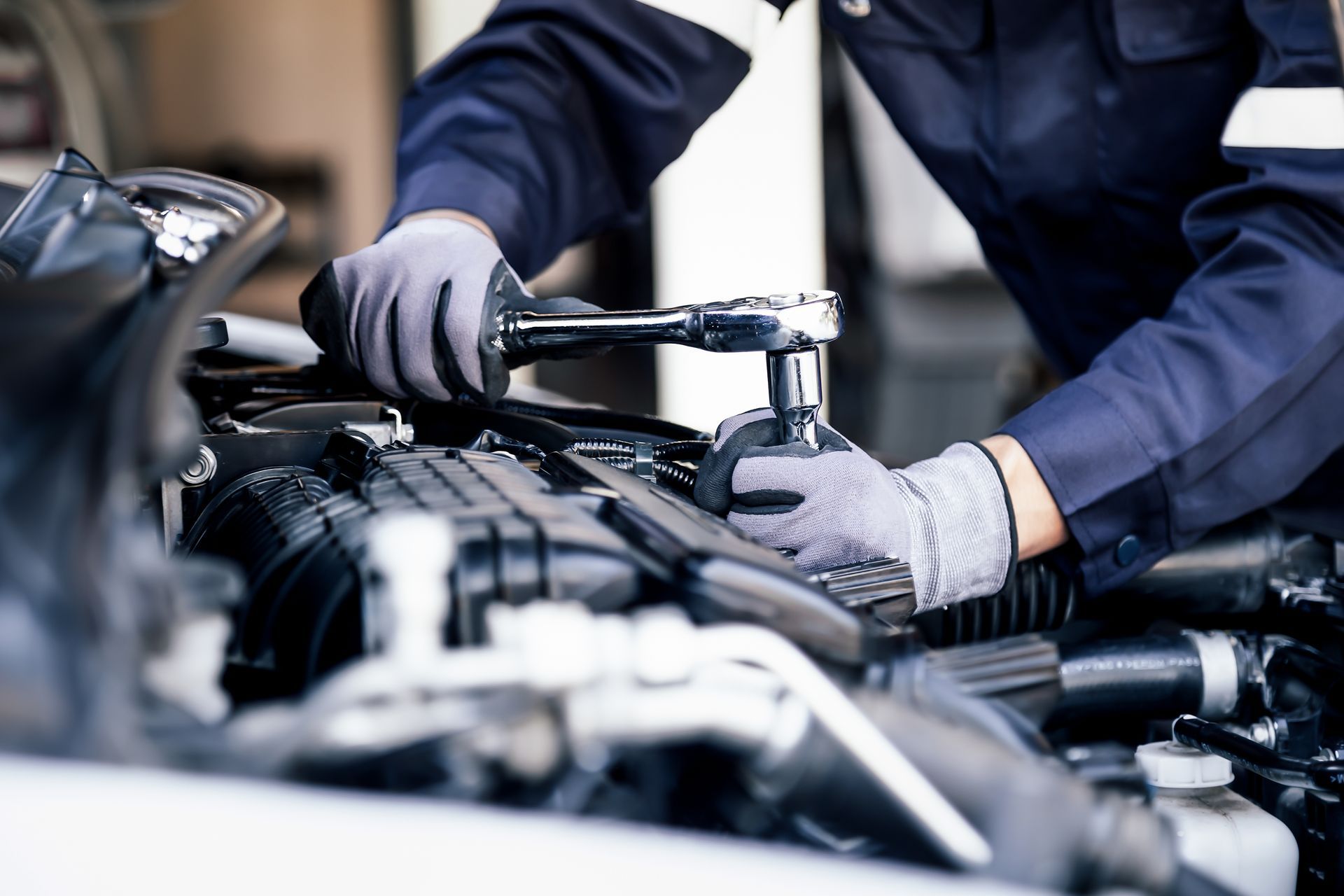 A mechanic is standing under a car on a lift in a garage.