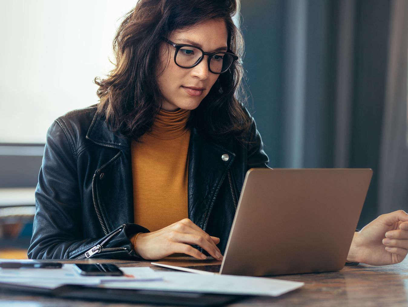 A woman is sitting at a desk using a laptop and a tablet.