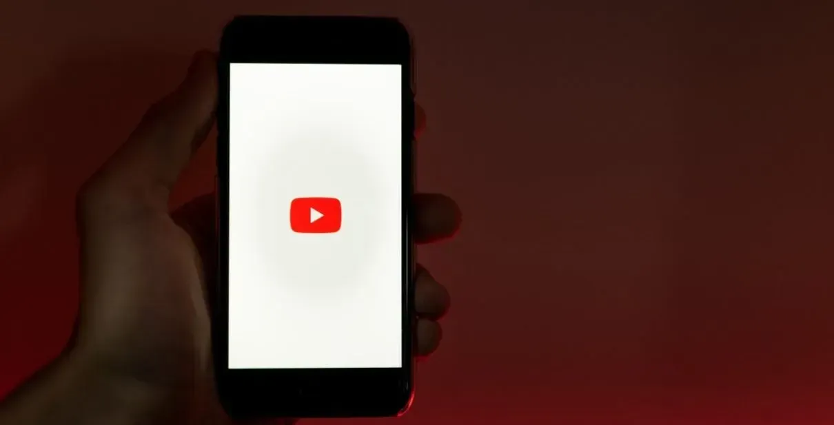 A person is holding a cell phone with a youtube logo on the screen.