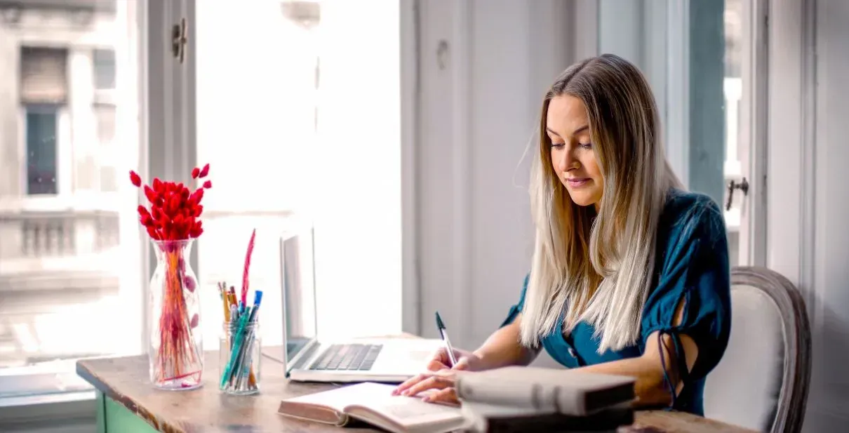 A woman is sitting at a desk writing in a notebook.