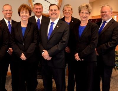 Group of seven people in black suits with blue accents, standing indoors.
