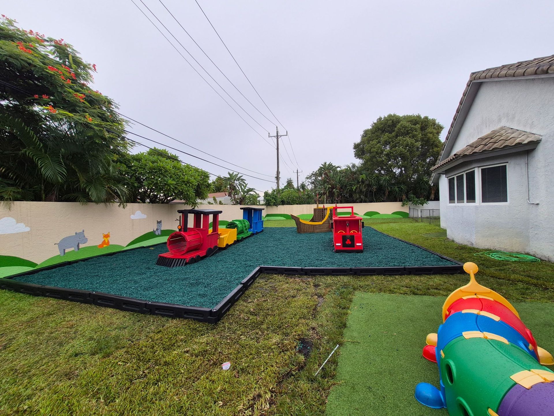 Playground with a train, truck, and ship on green rubber surfacing; grass surrounds.