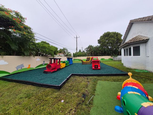 Playground with a train, truck, and ship on green rubber surfacing; grass surrounds.