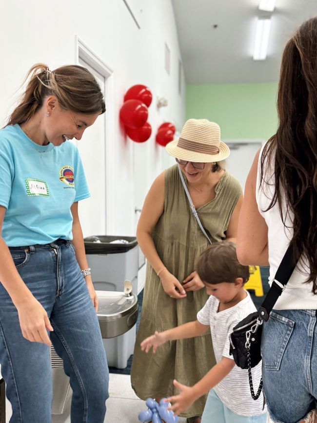 Woman in blue shirt smiles at child holding a blue balloon; other people in background.