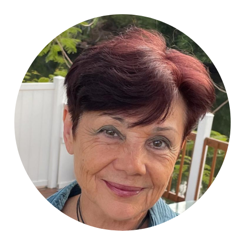 Woman with short auburn hair smiles, wearing a denim jacket, outdoors on a deck.