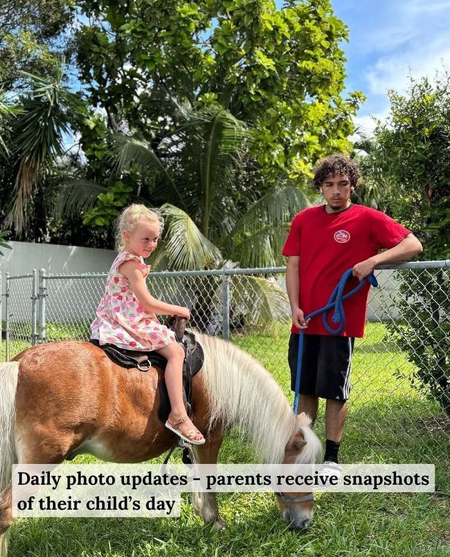 A young girl rides a pony as an adult holds the reins in a grassy outdoor area.