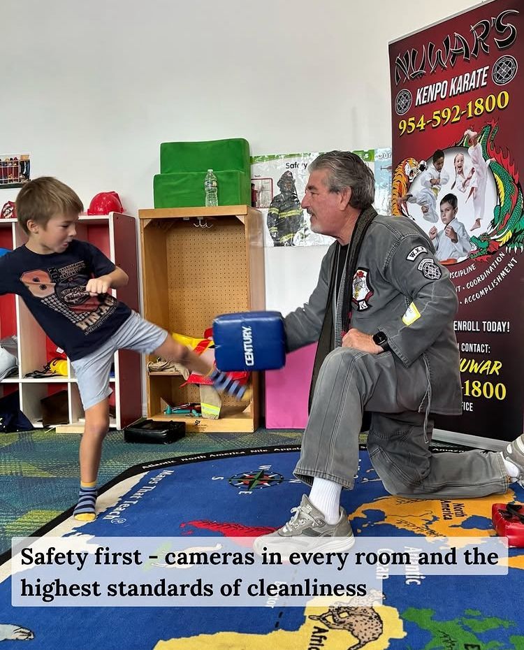 A child kicks a pad held by an instructor at AWWARS. The room has a rug, shelves, and cameras.