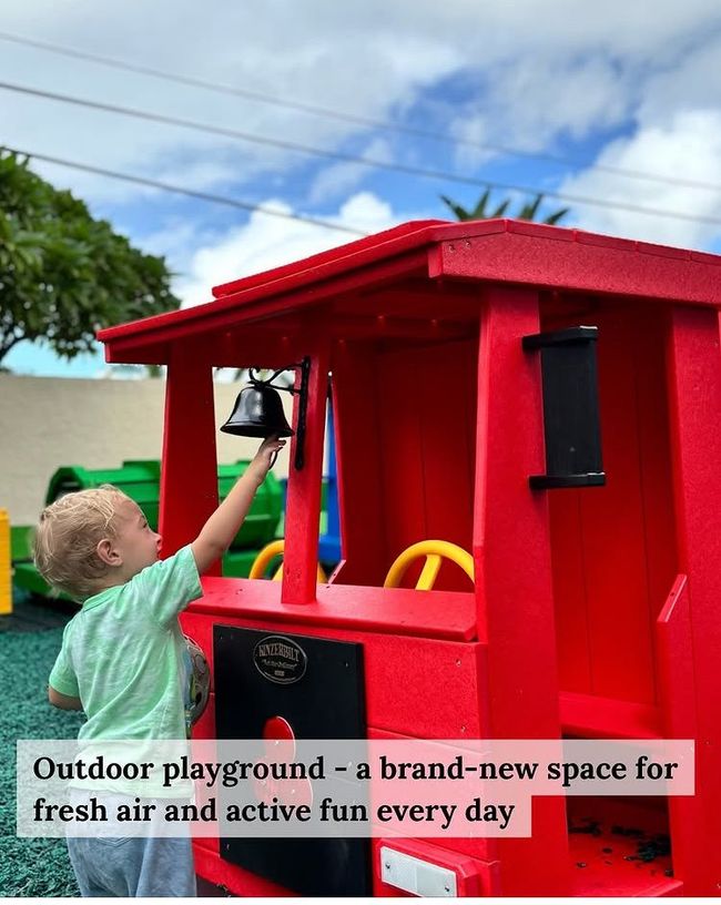 A young child rings a bell on a red train-shaped playground structure.