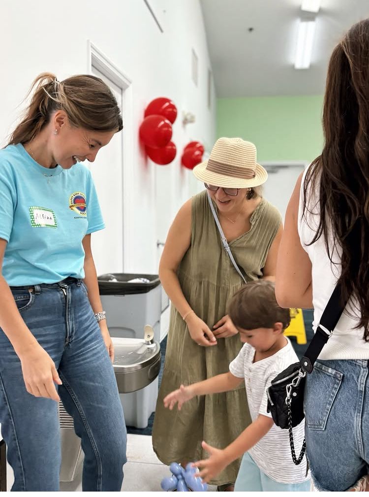 People in a room with balloons; a child reaches towards a woman.