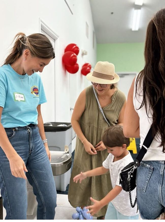 People in a room with balloons; a child reaches towards a woman.
